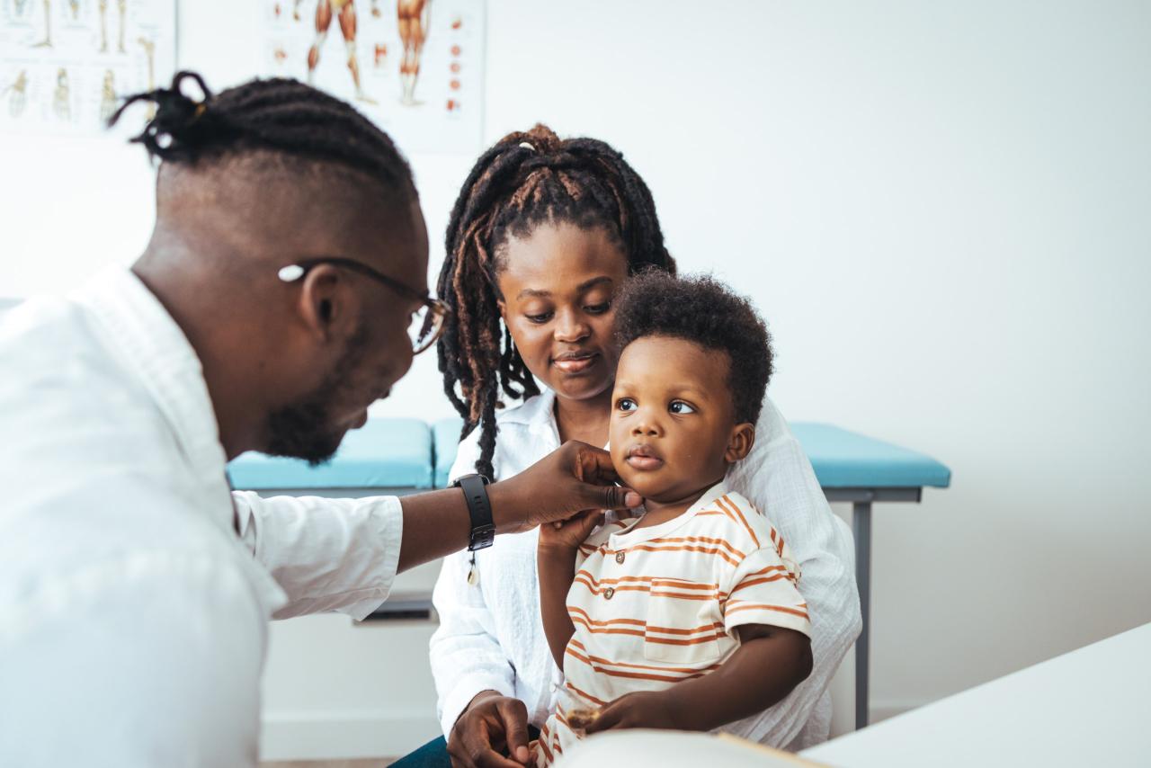 Pediatrician examining a toddler seated on his mother's lap