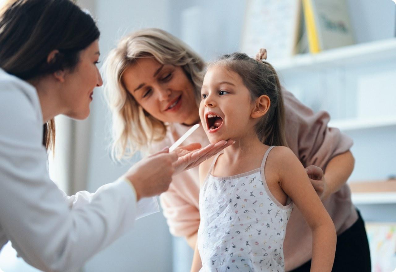 Pediatrician checking a young girl's throat while her mother looks on