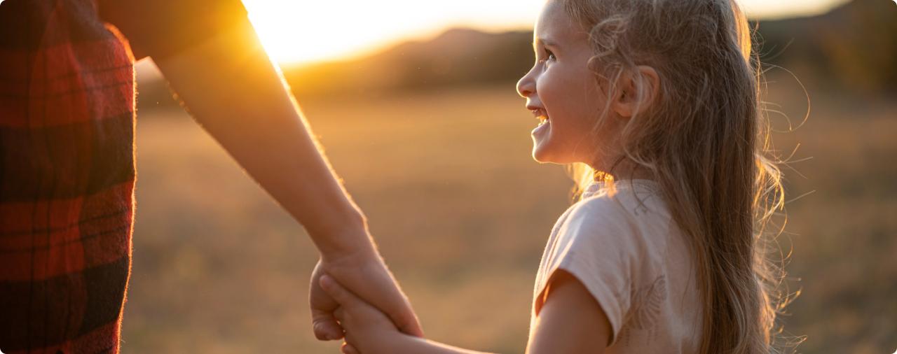 Smiling girl holding her parent's hand in a field at sunset