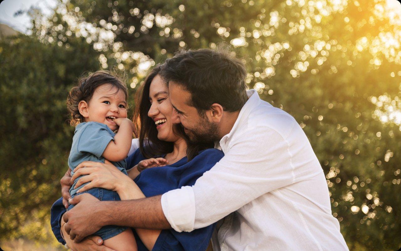 Parents cuddling their laughing toddler outdoors