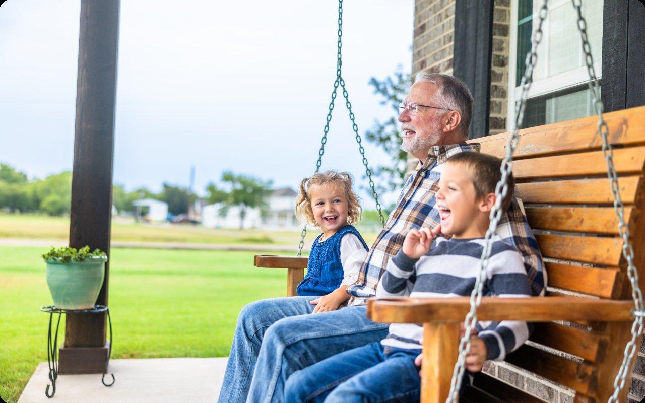 Grandfather laughing with two children on a porch swing