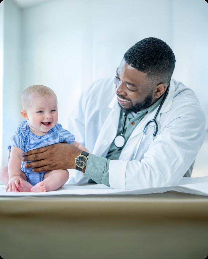Doctor steadying a smiling baby seated on an exam table