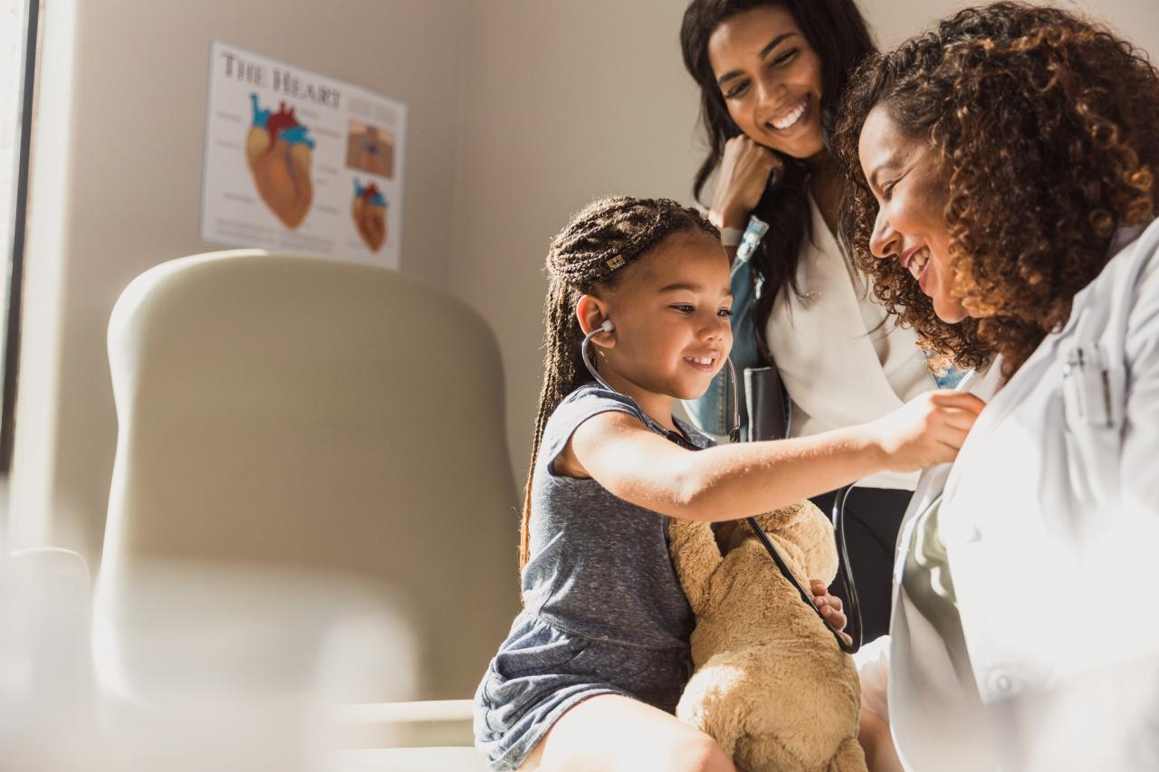 Girl listening through a stethoscope held to her pediatrician's chest