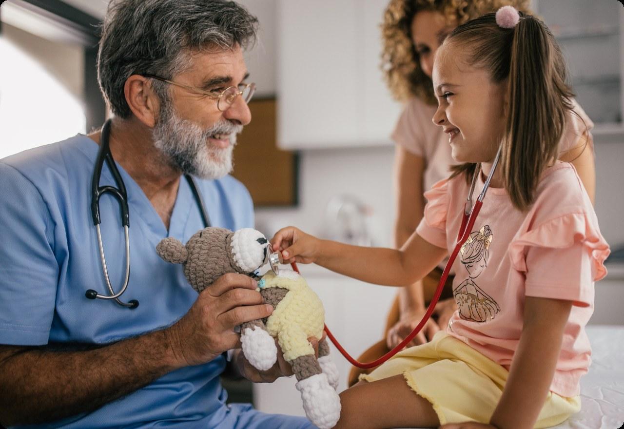Girl using a toy stethoscope on a teddy bear held by her pediatrician