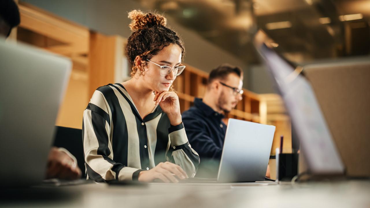 Two colleagues work at laptops in a shared office
